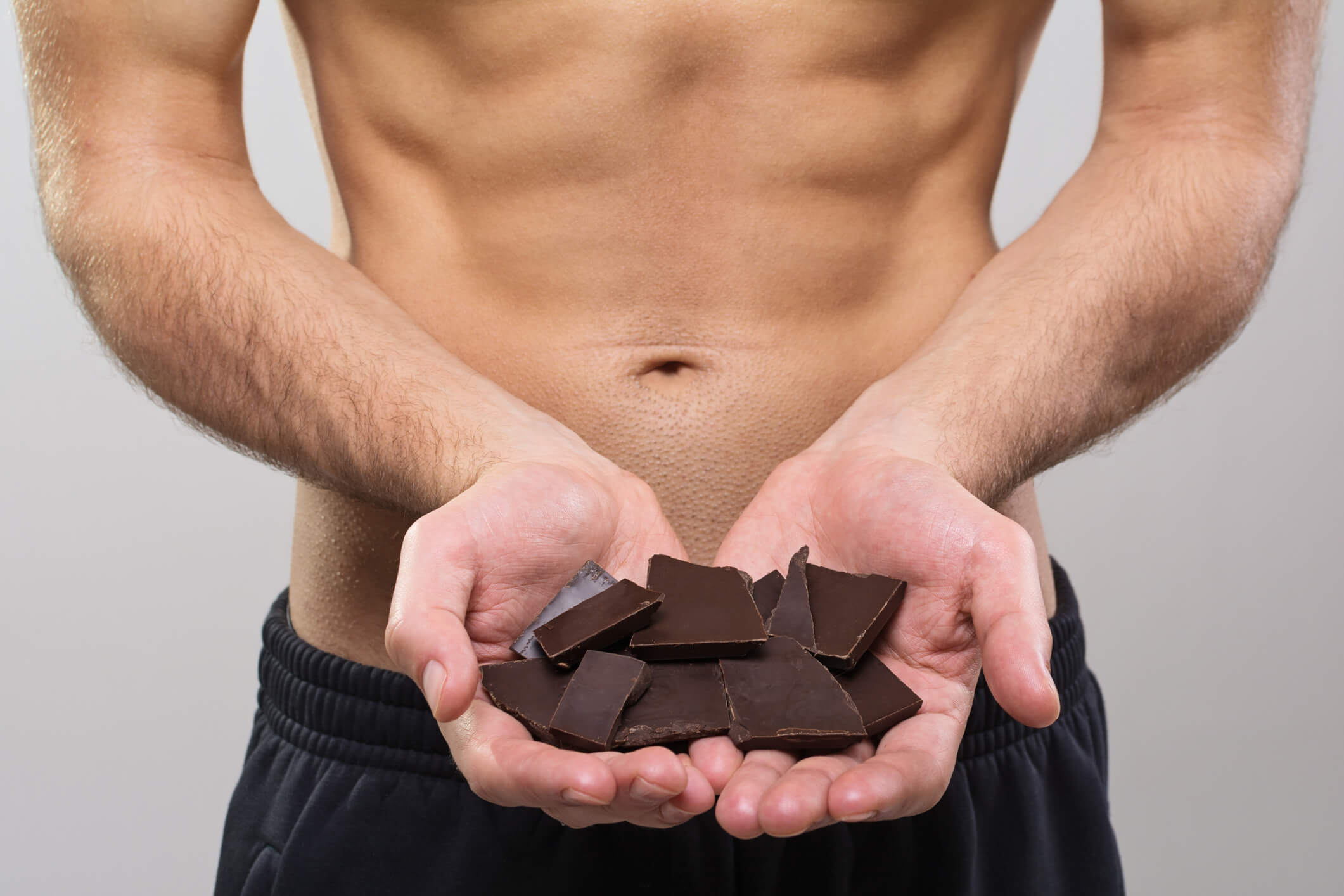 Man holding chocolate containing minimal sugar in order to achieve his six pack abs