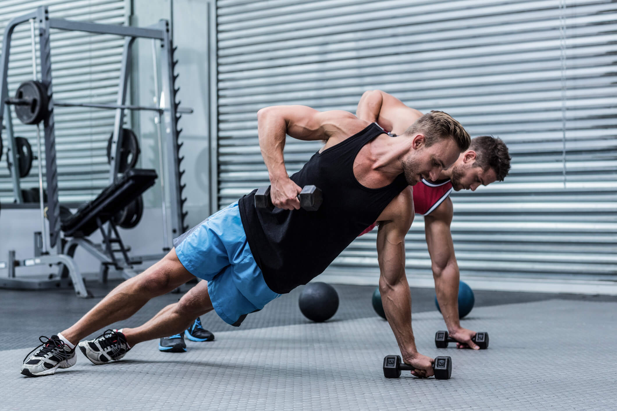 Muscular men doing a side plank while lifting a dumbbell